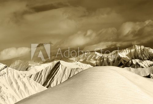 Sepia off-piste snowy slope and cloudy mountains