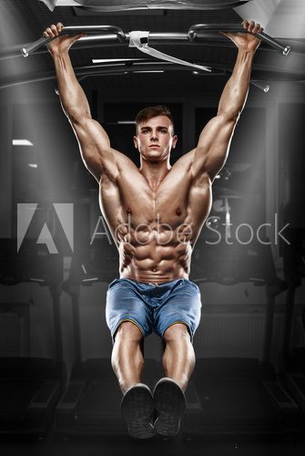 Muscular man working out in gym, doing stomach exercises on a horizontal bar, strong male naked torso abs