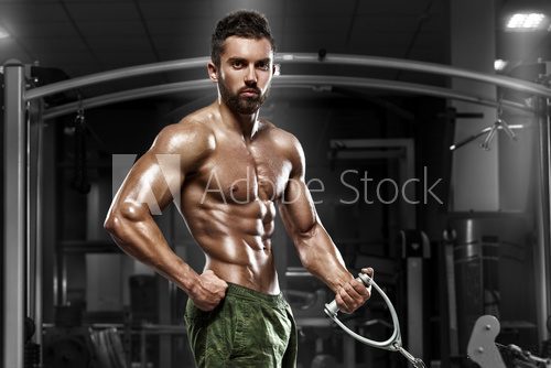 Muscular man working out in gym doing exercises at biceps, strong male naked torso abs