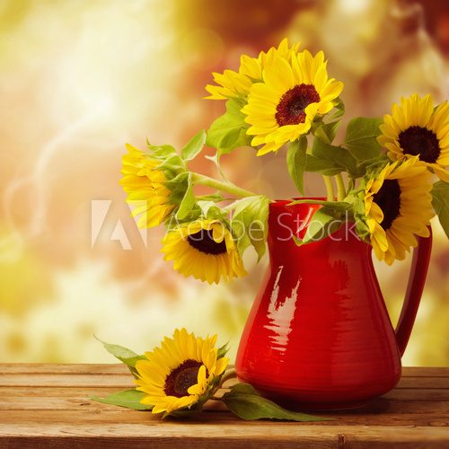 Sunflower bouquet in jug on wooden table over autumn bokeh