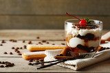 Tasty tiramisu dessert in glass, on napkin, on wooden 
