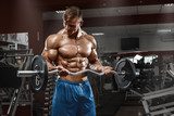 Muscular man working out in gym doing exercises with barbell at biceps, male naked torso abs