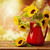 Sunflower bouquet in jug on wooden table over autumn bokeh 