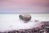 Romantic atmosphere in peaceful morning at sea. Big boulders sticking out from smooth wavy sea. Pink horizon