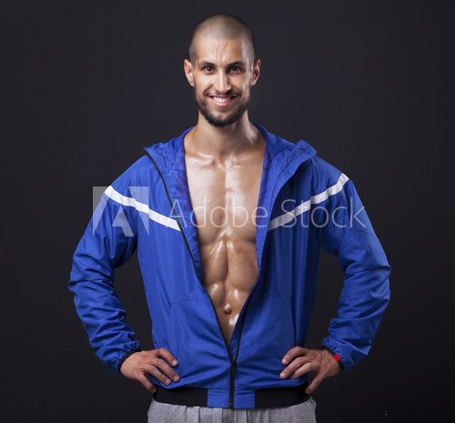Smiling athletic man showing six pack abs on black background