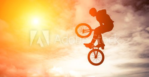 Man silhouette doing an jump with a bmx bike against sunshine sky.