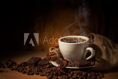Cup of coffee in coffee beans on brown background