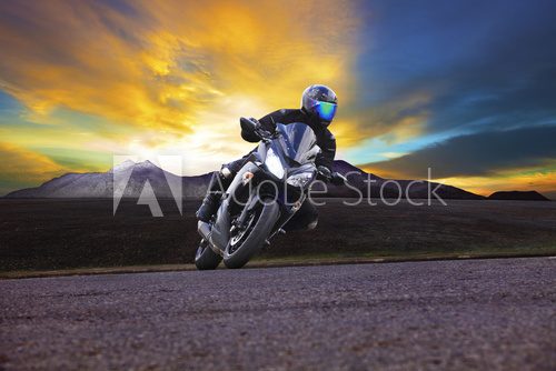 young man riding motorcycle in asphalt road curve with rural and