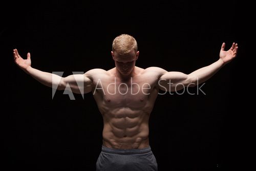 Athletic handsome man fitness-model is showing six pack abs. isolated on black background with copyspace