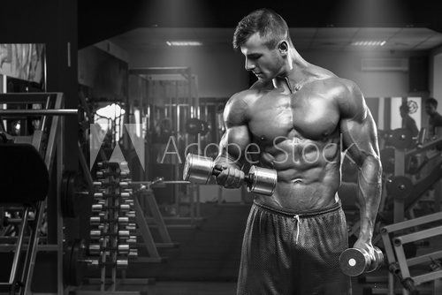Muscular man working out in gym doing exercises with dumbbells at biceps, strong male abs