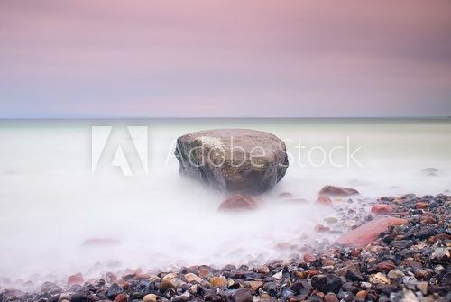 Romantic atmosphere in peaceful morning at sea. Big boulders sticking out from smooth wavy sea. Pink horizon