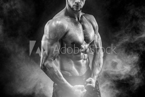 Strong bodybuilder with six pack. Man with perfect abs, shoulders,biceps, triceps and chest, personal fitness trainer flexing his muscles in smoke